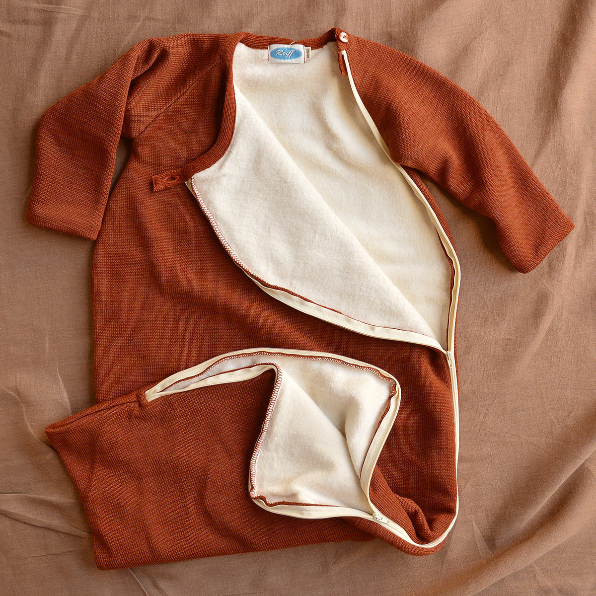 Brown baby wool sleeping bag with white lining on a brown background